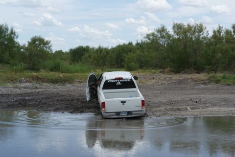 1989 Ford Bronco - White pickup truck stuck in mud and water with driver's door open.