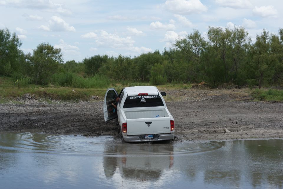 White pickup truck with driver's door open stuck in muddy water. Sticker on rear window reads "RIDING 4 WHEELERS"