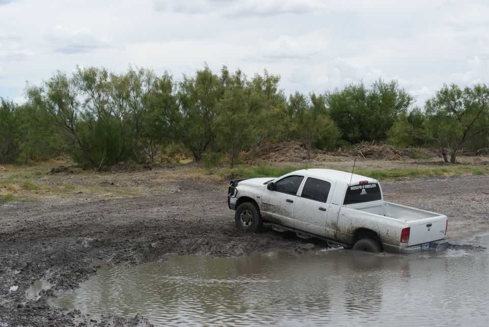 White pickup truck stuck in a muddy puddle, rear passenger side submerged