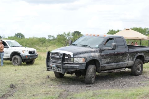 1989 Ford Bronco - Two pickup trucks are parked in a grassy, muddy area under a cloudy sky. A canopy is set up in the background.