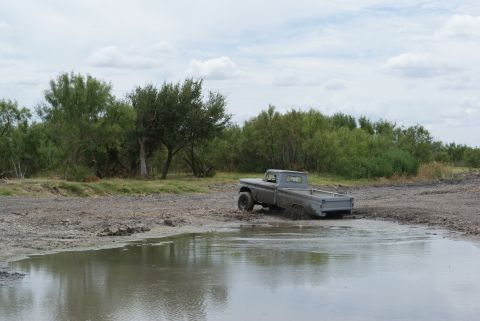 1989 Ford Bronco - Pickup truck stuck in mud hole with water and vegetation.