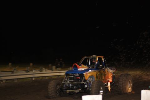 1989 Ford Bronco - A custom-built monster truck with a roll cage and large tires is seen on a dirt track at night.