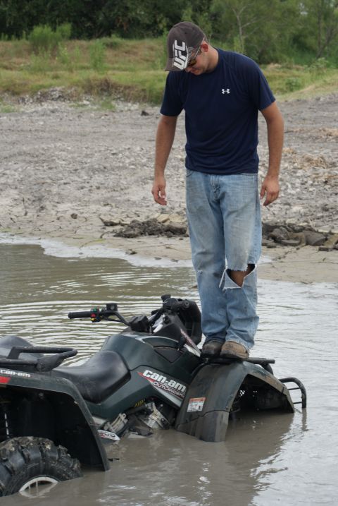 1989 Ford Bronco - A man stands on a stuck Can-Am Outlander ATV in a muddy waterhole.