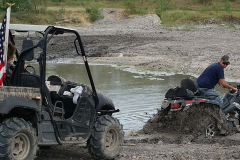 1989 Ford Bronco - Two off-road vehicles, a UTV and an ATV, are stuck in the mud near a body of water.