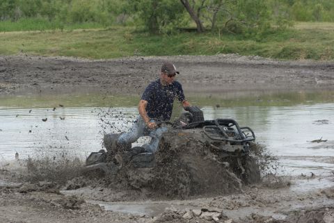 1989 Ford Bronco - Rider navigates an ATV through a muddy water obstacle, creating a large splash.