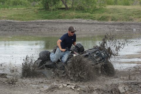 1989 Ford Bronco - An ATV navigates through a muddy obstacle, sending mud and water flying.
