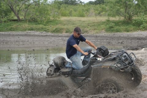 1989 Ford Bronco - A rider navigates an ATV through a muddy, watery terrain, kicking up a significant splash.