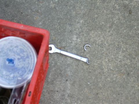 1991 Ford Bronco - A chrome combination wrench and a small C-shaped retaining clip lie on a gray concrete driveway next to the corner of a red plastic crate h…