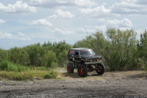 1989 Ford Bronco - This modified truck is kicking up dust as it drives through a muddy, outdoor area with sparse vegetation.