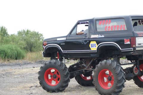1989 Ford Bronco - Modified black monster truck with "WOOD CONTROL" text on the window sits on a dirt lot.