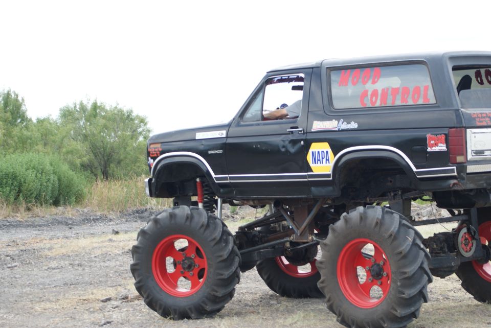 Black monster truck with red rims and large tires, lifted suspension, side view. "WOOD CONTROL" text on rear window