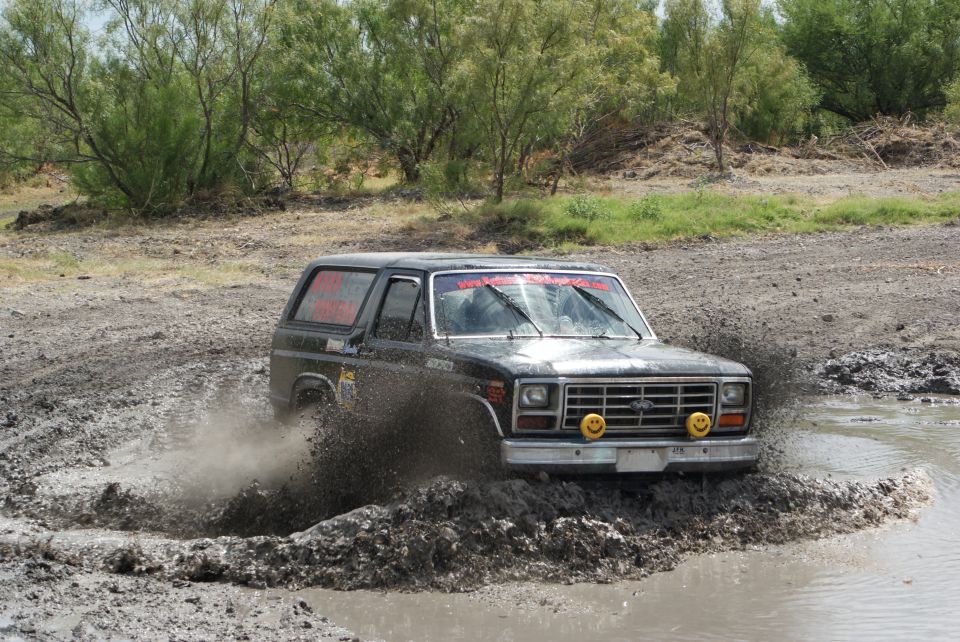 Black Ford Bronco splashing through a mud pit. Has smiley face lights on the front