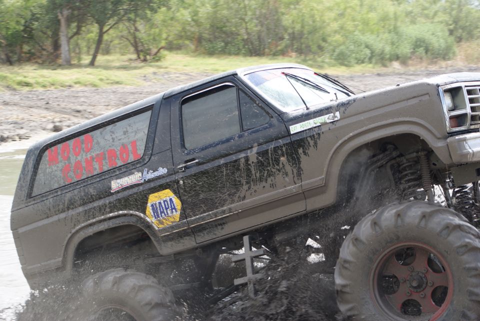 1989 Ford Bronco with "WOOD CONTROL" on the rear window driving through mud