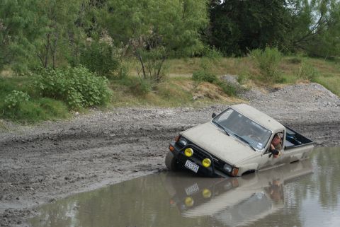 1989 Ford Bronco - A Toyota pickup truck is stuck in a muddy body of water, with the front tires and lower body submerged.