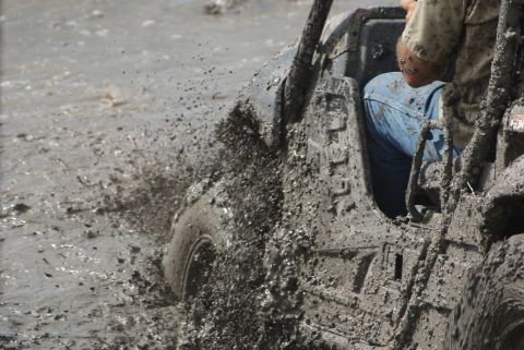 1989 Ford Bronco - An off-road vehicle navigates a muddy terrain, kicking up spray as it moves.