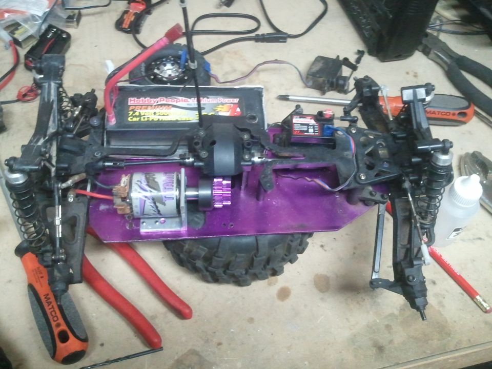 RC car chassis with purple frame, electric motor, battery, and suspension parts. Tools are on the workbench