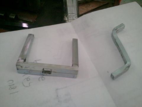 1985 Ford Bronco - Two metal parts, a bracket and a bent tool, are shown on a surface with some handwritten numbers and a SuperMotors logo.