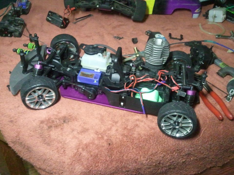 RC car chassis with engine, purple frame, and silver wheels on a red towel