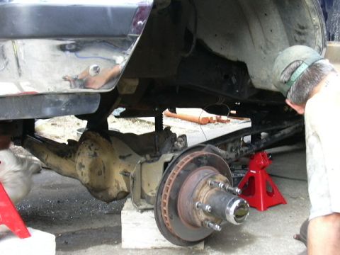1991 Ford Bronco - Mechanic inspects the rear axle and suspension of a vehicle elevated on jack stands during a lift kit installation.