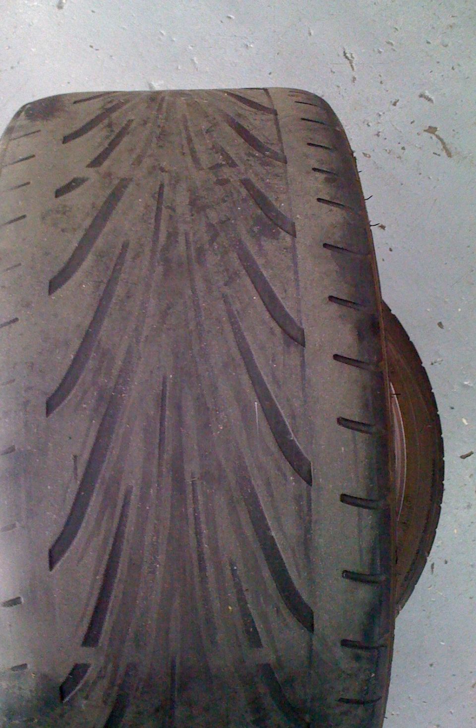 Close-up of a worn directional performance tire tread on a concrete floor