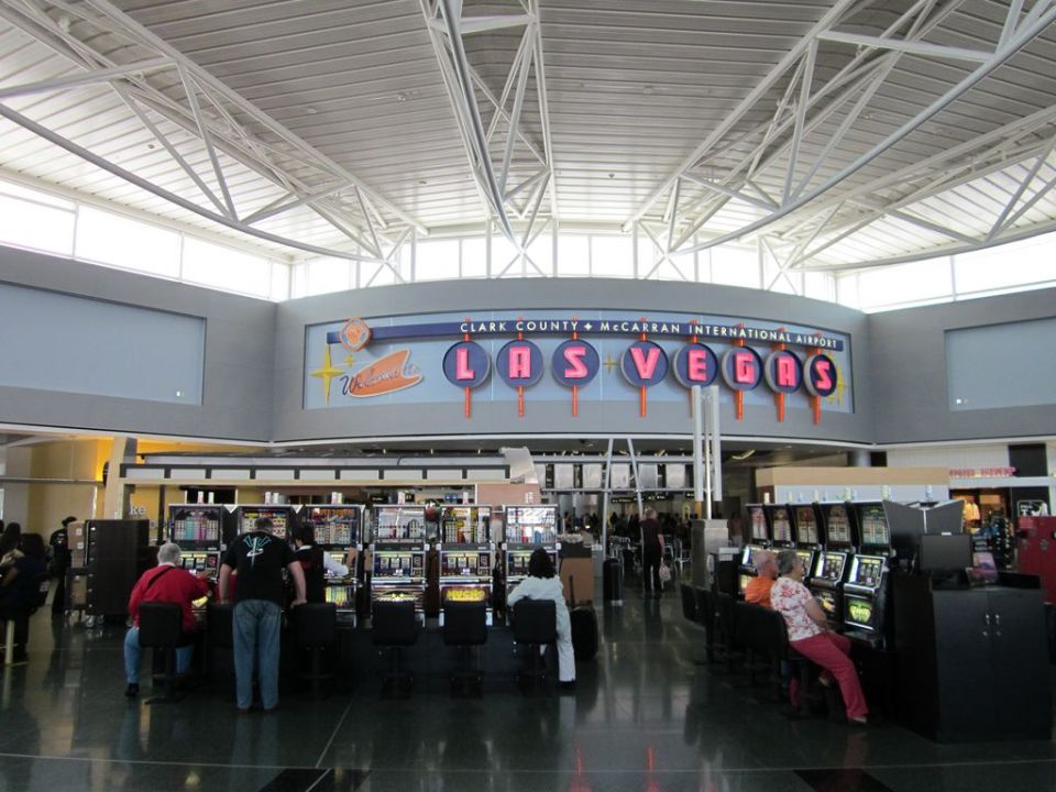 Interior of Clark County + McCarran International Airport terminal with rows of slot machines and people playing