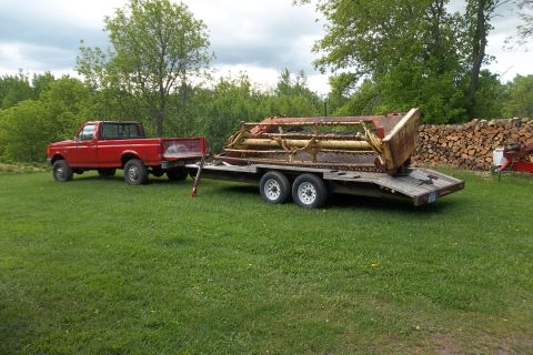 1987 Ford F-250 - A red 1987 Ford F-250 pickup truck is parked on a grassy field, hitched to a trailer carrying agricultural machinery.