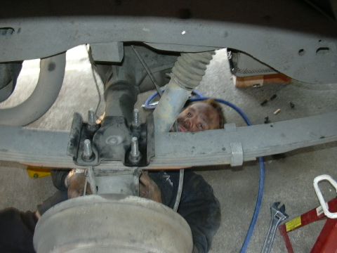 1991 Ford Bronco - A mechanic is seen working on the underside of a vehicle, focusing on the rear axle and suspension system.