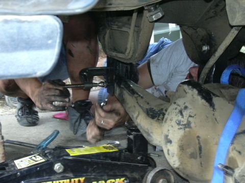 1991 Ford Bronco - Mechanics work on vehicle suspension components, using clamps and a jack.
