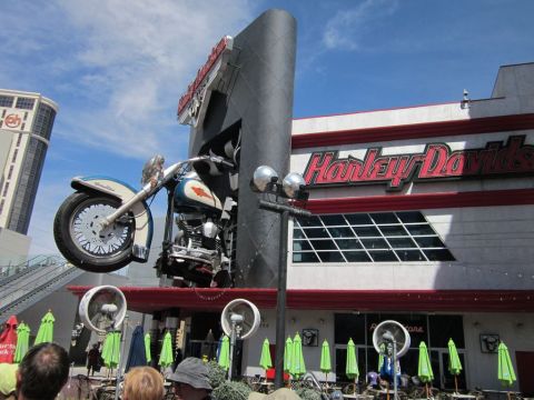 1991 Ford LTD Crown Victoria - A large motorcycle sculpture is mounted on the exterior of a Harley-Davidson building, with people visible in the foreground.