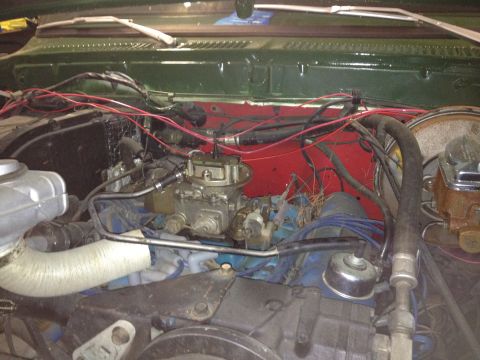 1978 Ford Bronco - Engine bay of a vehicle, showing the carburetor and various hoses and wires against a red firewall.