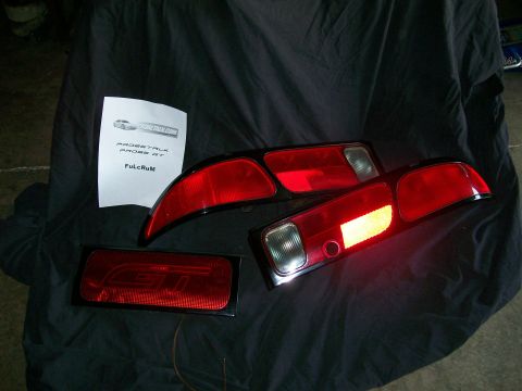 1995 Ford Probe - Ford Probe GT taillights are laid out on a black cloth surface with a document.