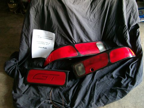 1995 Ford Probe - A set of red car tail lights and a GT emblem are laid out on a black cloth, with a paper document nearby.