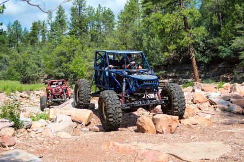 1966 Ford Bronco - Two custom off-road buggies traverse a challenging, rocky trail surrounded by trees.