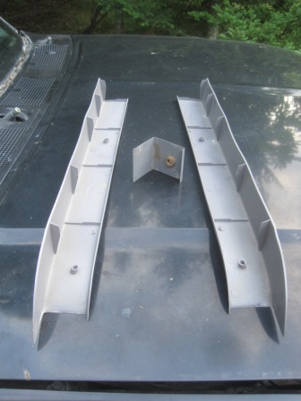 1993 Ford Bronco - Two silver trim pieces and a metal bracket are laid out on the hood of a dark vehicle.