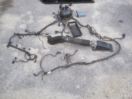 1993 Ford Bronco - Wiring harness and air intake parts from a Ford Bronco are spread out on a concrete surface.