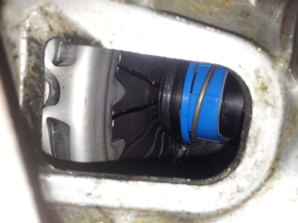 Close-up of a black hose with blue plastic bands and a metal spring, viewed through an opening in a metal housing