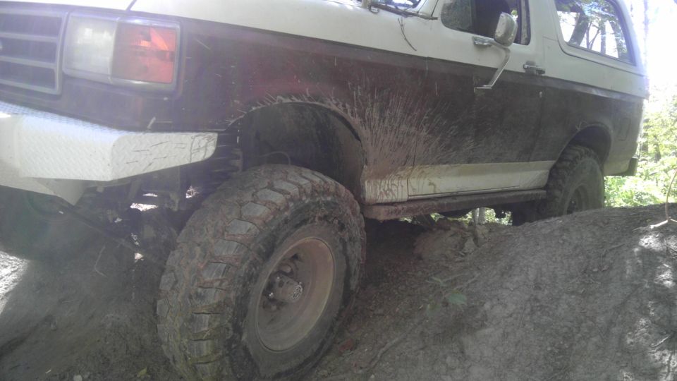 Ford Bronco climbing over dirt and mud, front wheel visible