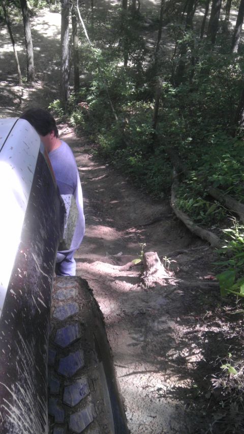 1989 Ford Bronco - A person stands next to a white vehicle on a narrow, muddy path through a dense forest.