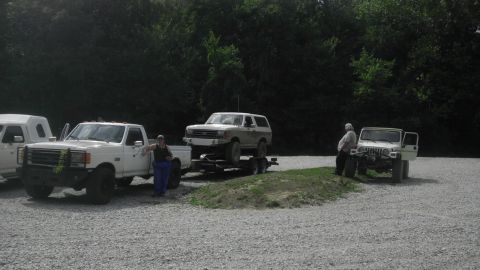 1989 Ford Bronco - A white Ford Bronco is loaded onto a trailer, with a pickup truck and a Jeep also present in the lot.
