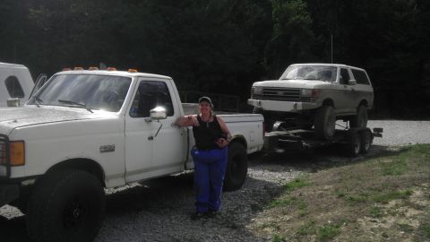 1989 Ford Bronco - A white Ford pickup truck tows a white Ford Bronco on a trailer.