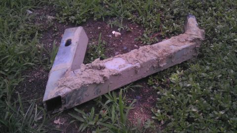 1989 Ford Bronco - A metal component, heavily coated in mud, lies on the ground amidst grass and dirt.