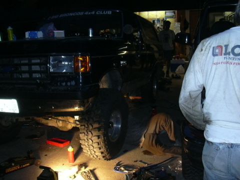 1991 Ford Bronco - Mechanics work on a 1991 Ford Bronco in a garage, illuminated by work lights.