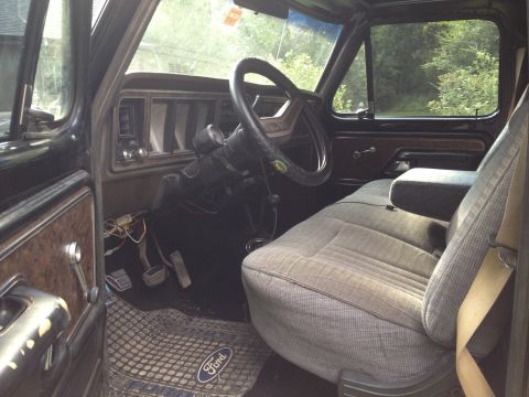 1979 Ford Bronco - The interior of a truck shows the driver's seat, dashboard, and steering wheel. A Ford logo is visible on the floor mat.