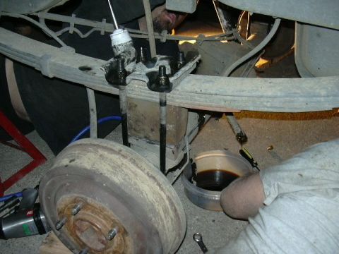 1991 Ford Bronco - Close-up view of a vehicle's rear suspension system during a repair, with a mechanic attending to the leaf springs and shock absorber.