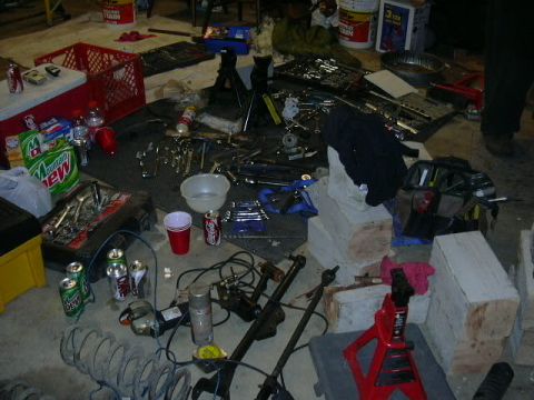 1991 Ford Bronco - A messy garage scene with various tools, car parts, and discarded beverage cans scattered across the floor.