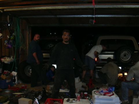 1991 Ford Bronco - Mechanics work on a lifted 1991 Ford Bronco in a cluttered garage.