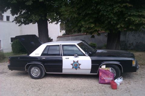 1991 Ford LTD Crown Victoria - This 1991 Ford Crown Victoria police car is seen from the side with its trunk ajar and shopping bags nearby.