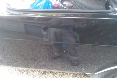 1991 Ford LTD Crown Victoria - A black car's side and open trunk are visible, reflecting a person and a spare tire.