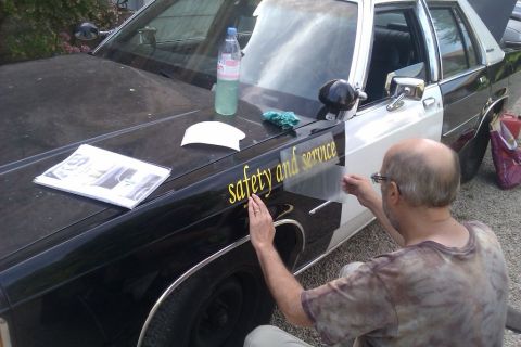 1991 Ford LTD Crown Victoria - A man applies a 'safety and service' decal to the side of a black and white 1991 Ford Crown Victoria.