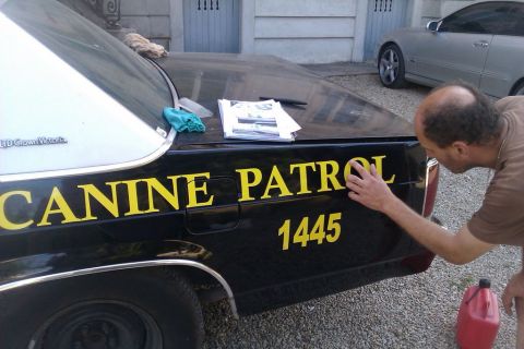 1991 Ford LTD Crown Victoria - A man cleans the lettering on a black 1991 Ford Crown Victoria police car, with another car visible in the background.